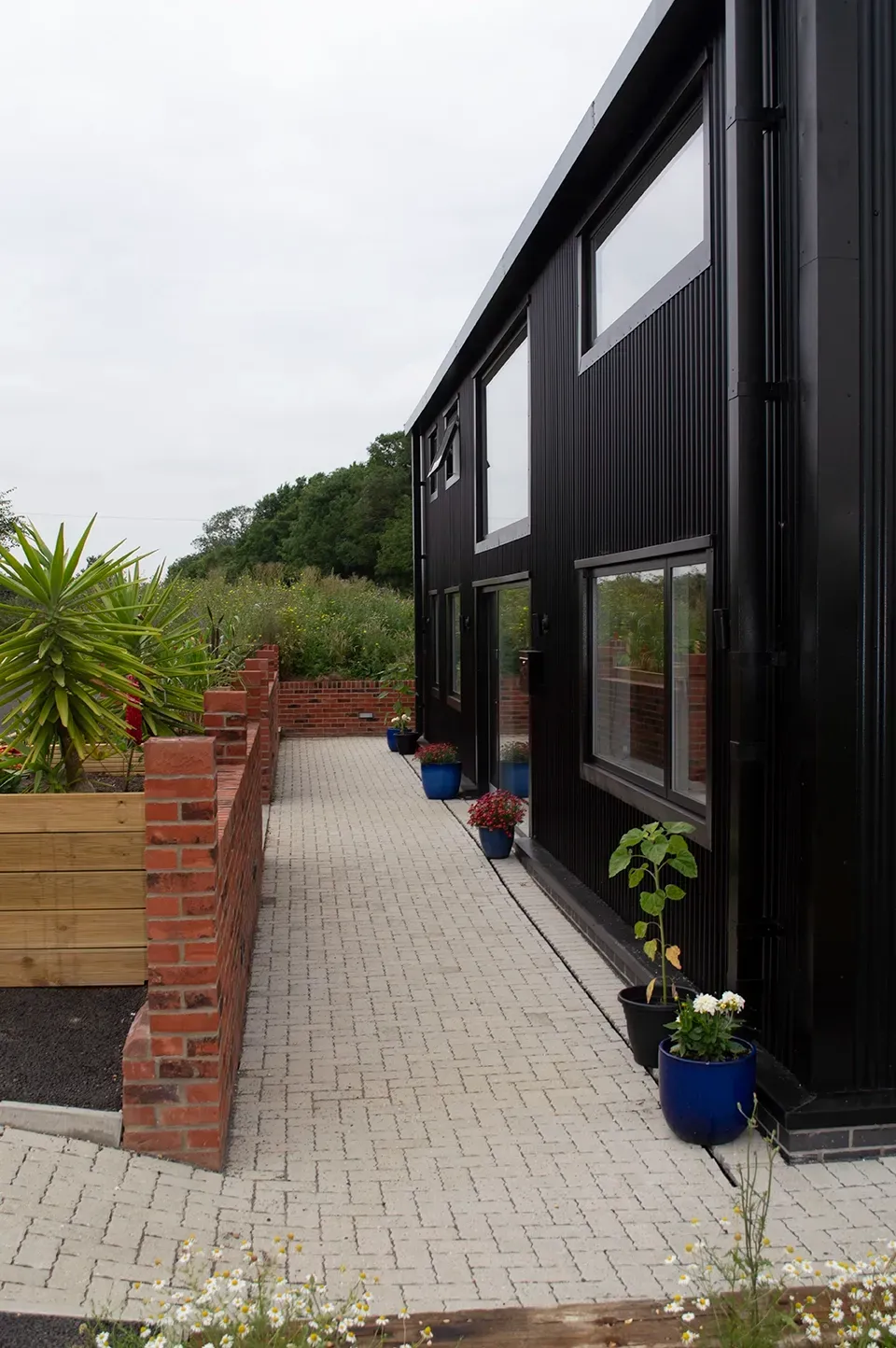 A black building with a brick wall and potted plants on the sidewalk.