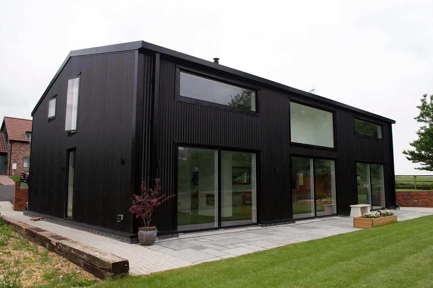 A large black house with a lot of windows is sitting on top of a lush green field.