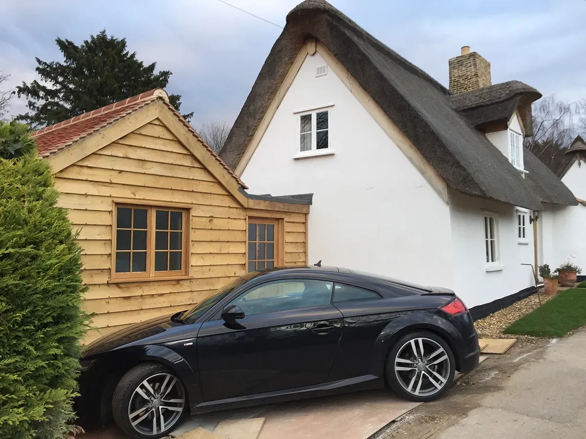A black car is parked in front of a thatched house