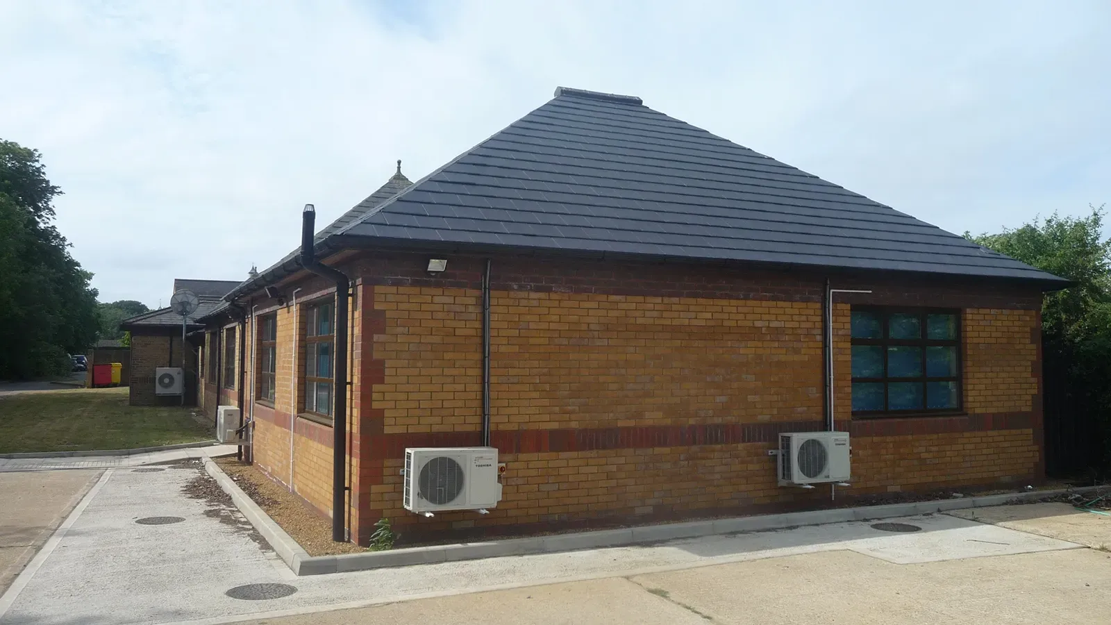 A brick building with a black roof and two air conditioners on the side.