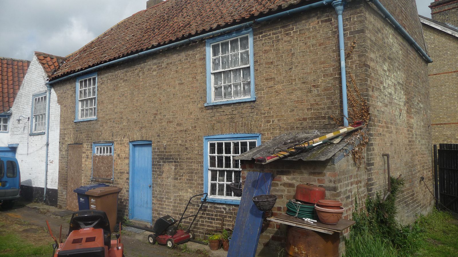 A brick house with a blue door and a lawn mower in front of it.