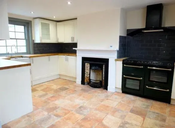 An empty kitchen with a black stove and a fireplace.