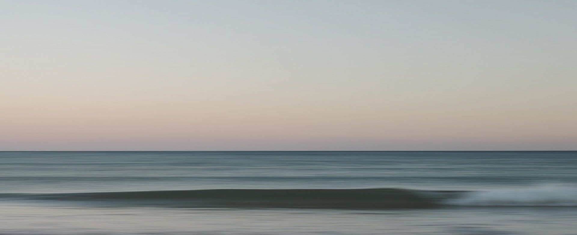 Océano en calma al amanecer con un cielo de tonos rosa pastel y azul sobre aguas tranquilas.