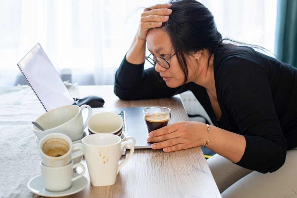 woman sits at a table with a laptop and two coffee cups, focused on her work