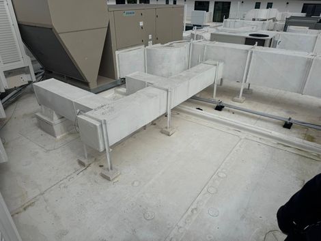 White HVAC ductwork runs across a flat rooftop near a large air conditioning unit and conduit piping.