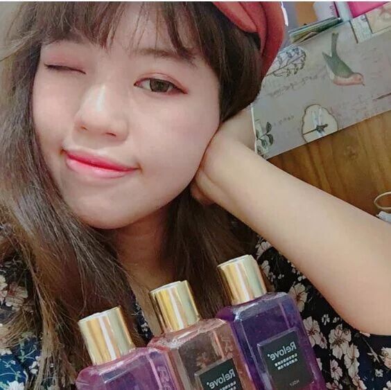 一個人眨眨眼睛,面帶微笑,手裡拿著三個帶有金色瓶蓋的香水瓶。