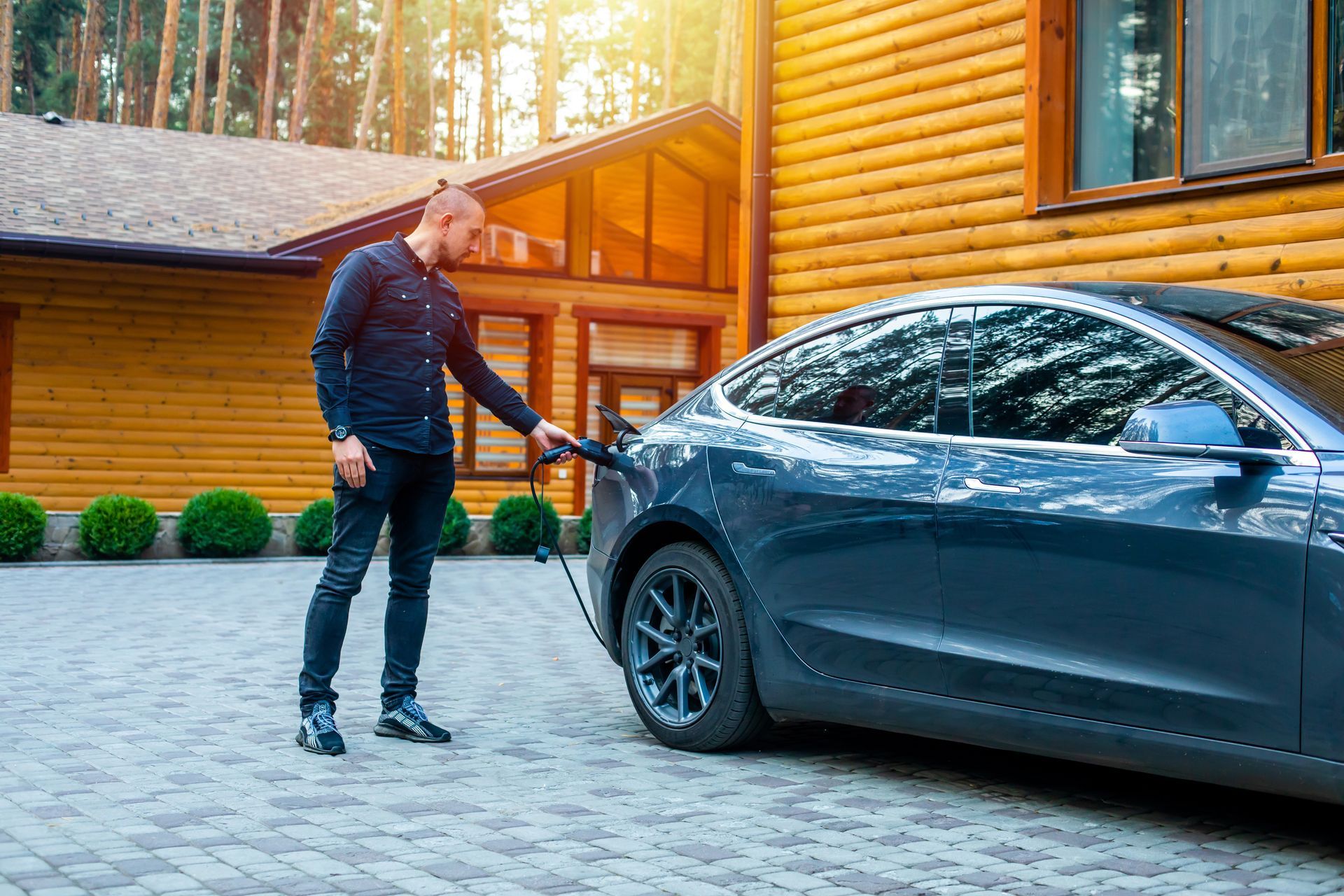 A man connecting a charging cable to a car from an electric car charging station by a townhouse. A man connecting a charging cable to a car from an electric car charging station by a townhouse.
