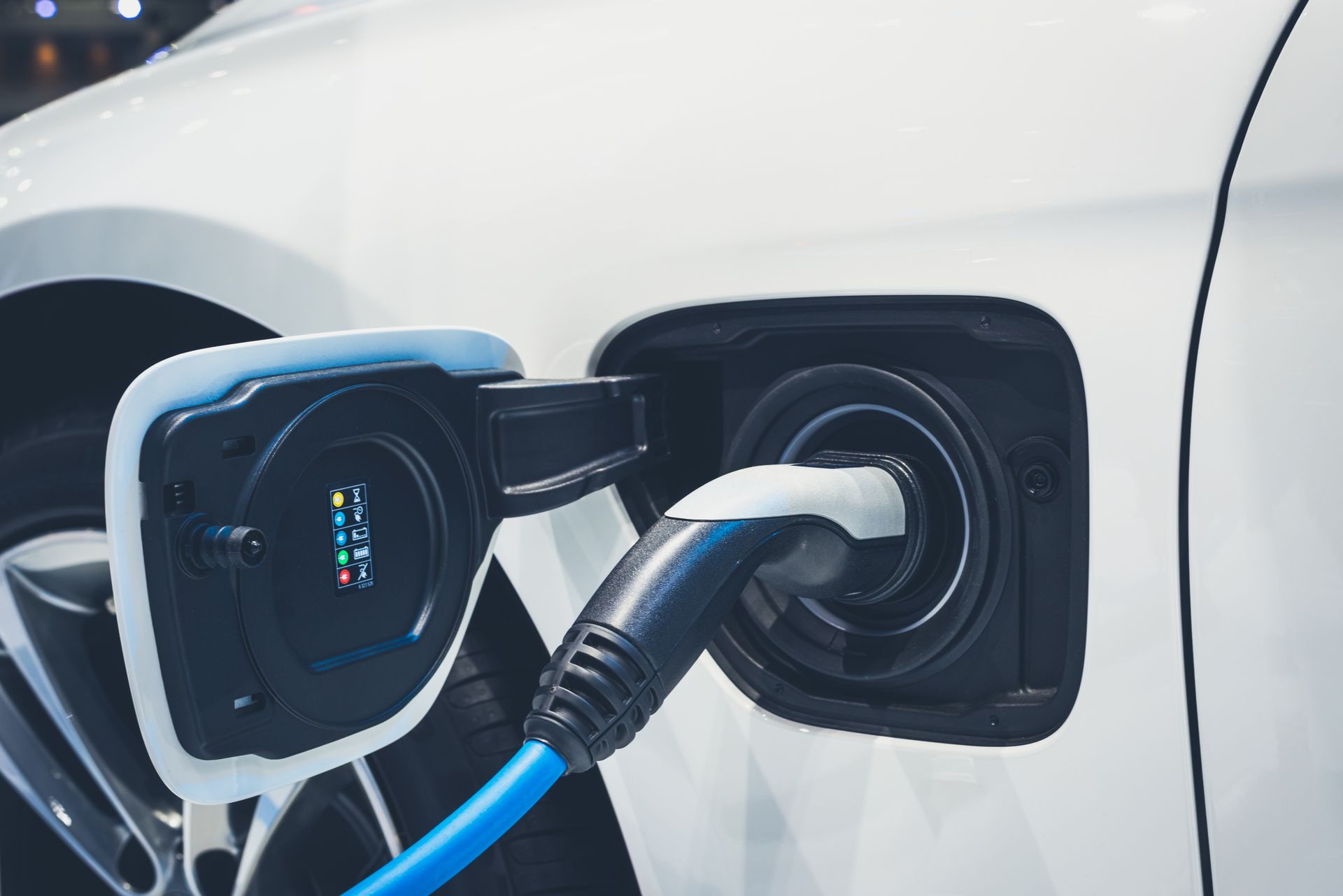 Close-up of a white electric vehicle being charged, the charger placed in its charging socket.