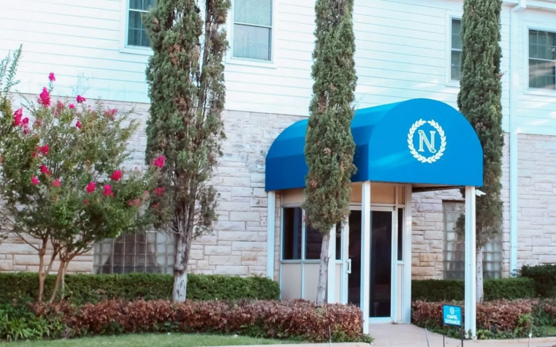 Building entrance with blue awning, white columns, and landscaped shrubs outside.