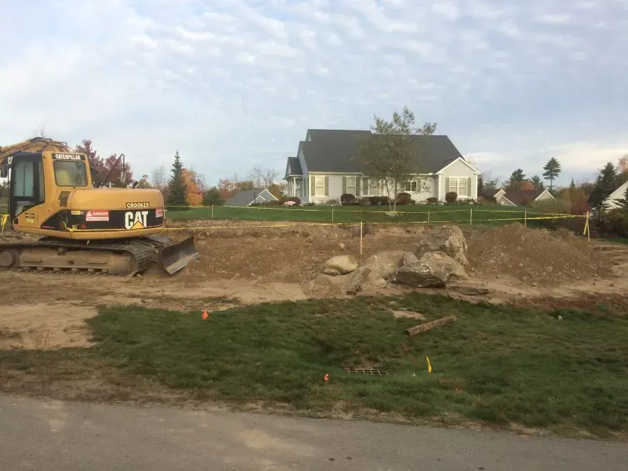 A construction site with a house in the background and a bulldozer in the foreground.