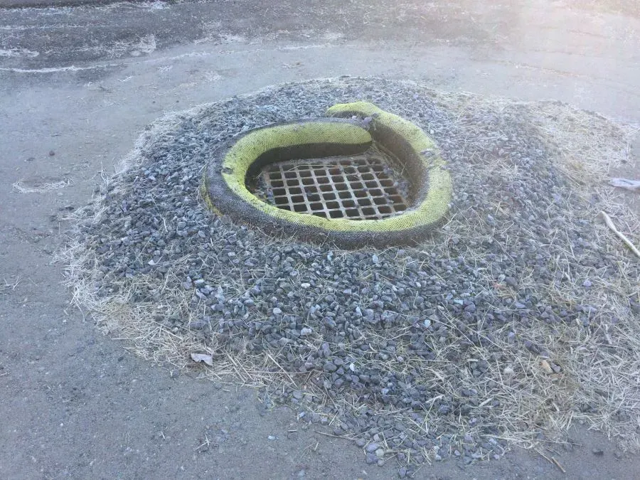 A manhole cover is sitting in the middle of a gravel area.