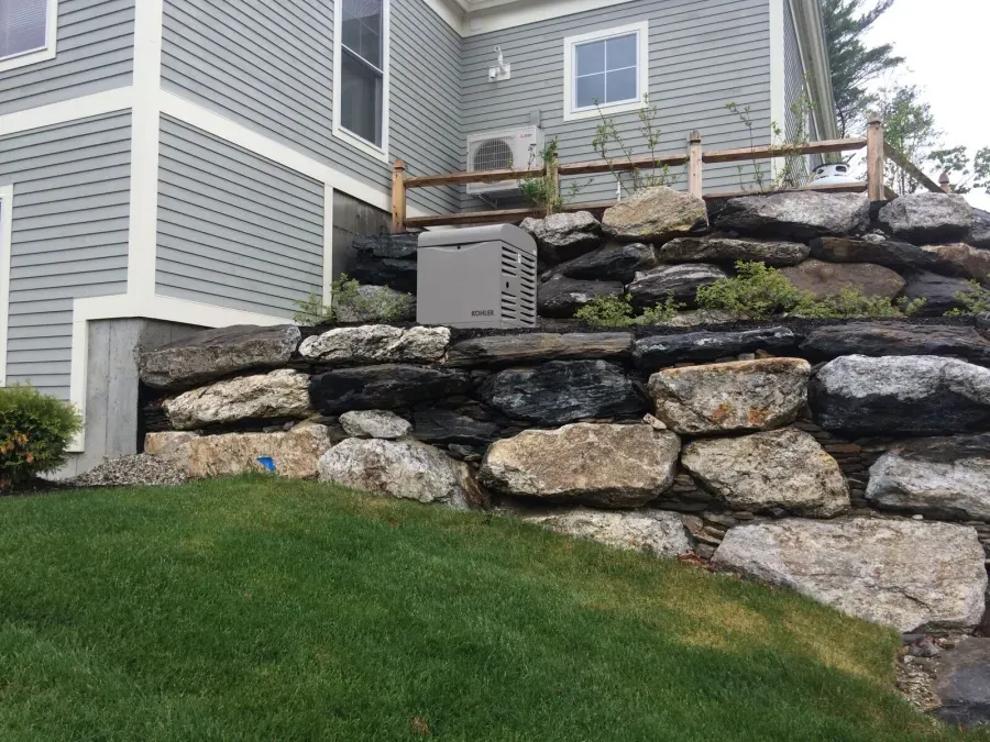 A large rock wall is in front of a house.