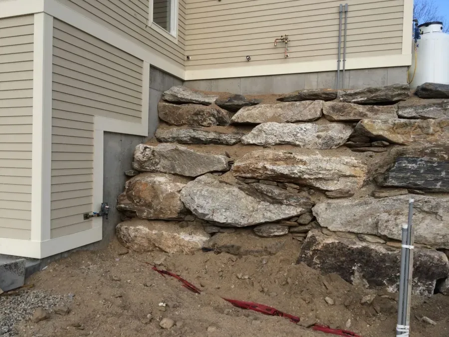 A large rock wall is being built in front of a house