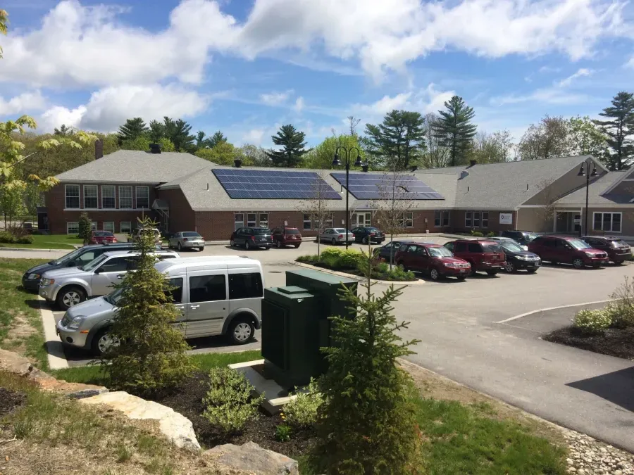 A row of cars are parked in front of a building with solar panels on the roof.