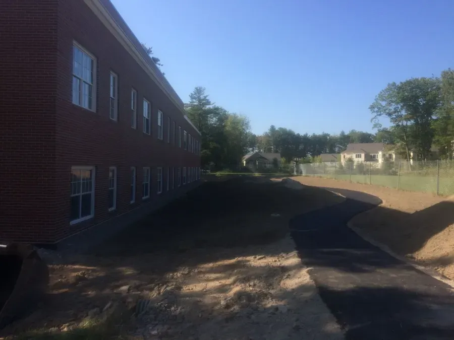 A brick building with a lot of windows is next to a dirt road.