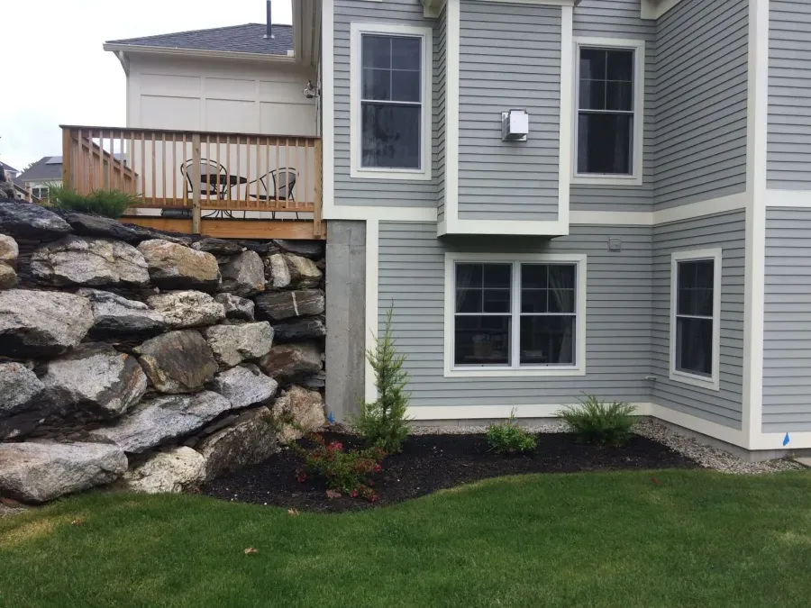 The back of a house with a large rock wall and a deck.