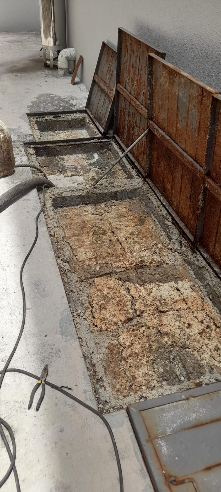 Canaletas metálicas oxidadas se alineaban a lo largo de una acera junto a un muro, llenas de tierra y escombros.