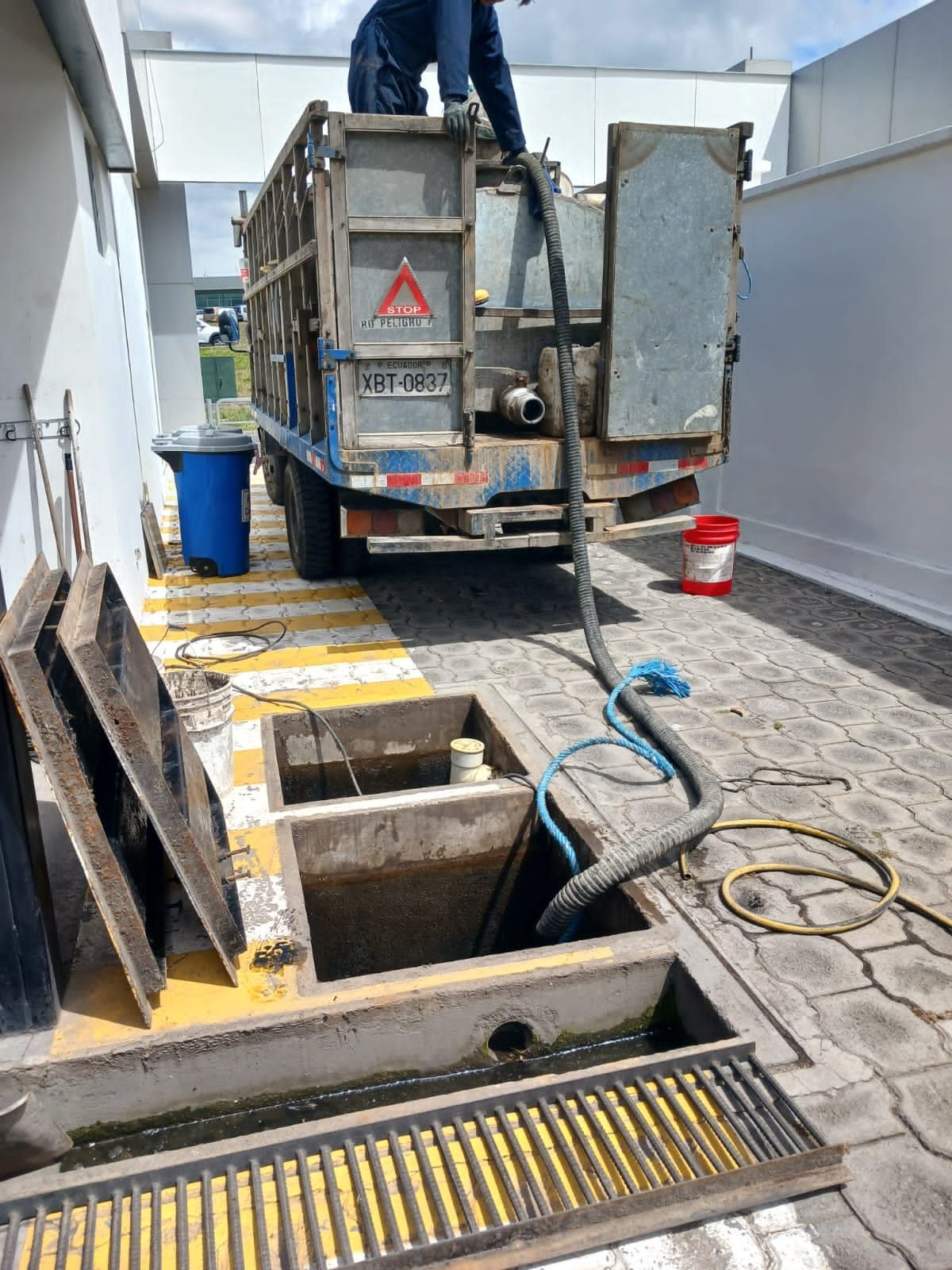 Camión de servicios públicos en una zanja de calle con tapas de alcantarilla abiertas, mangueras y herramientas de trabajo en un área pavimentada.
