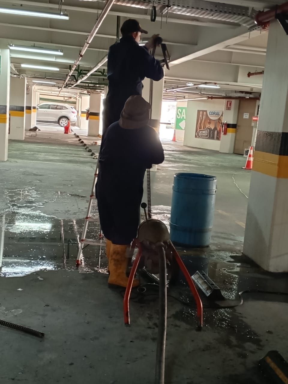 Una persona usa un trípode para cámara en un estacionamiento subterráneo, con un barril azul cerca.