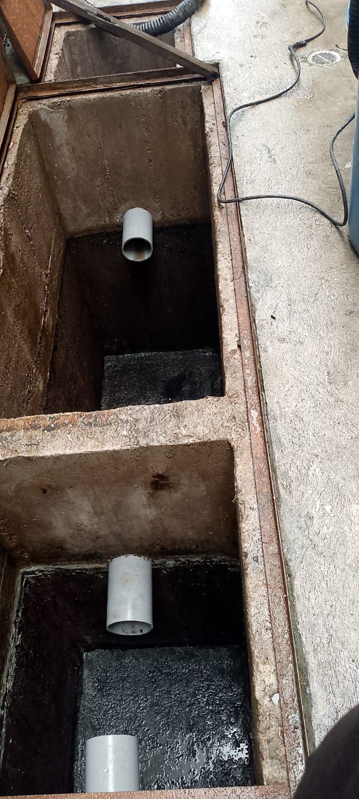 Primer plano de un desagüe o pozo de servicios oxidado con tres tuberías cortas de color gris dentro de compartimentos de hormigón.