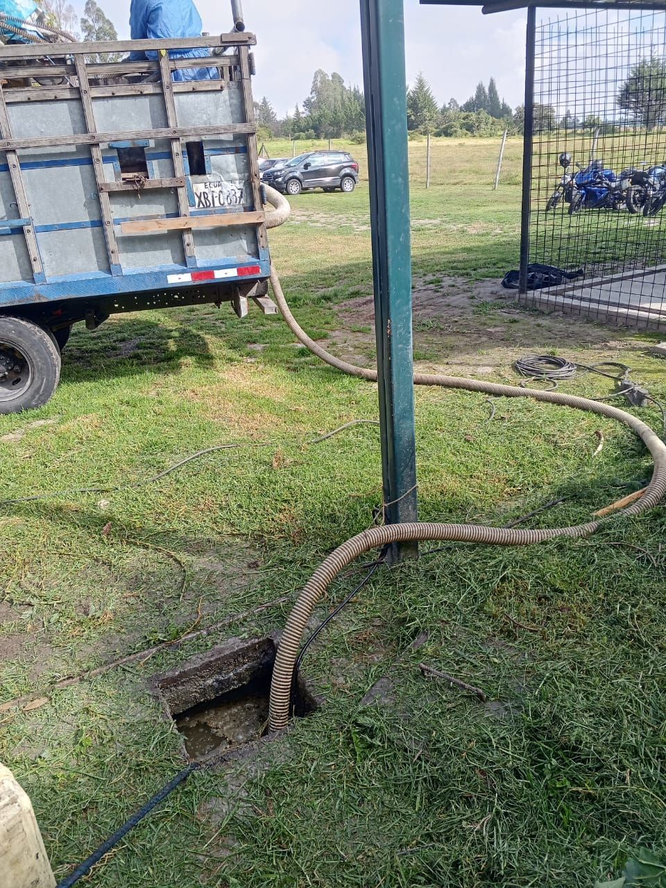 Camión con mangueras en un sitio de trabajo al aire libre cubierto de hierba cerca de un poste de servicios públicos y un agujero en el suelo.
