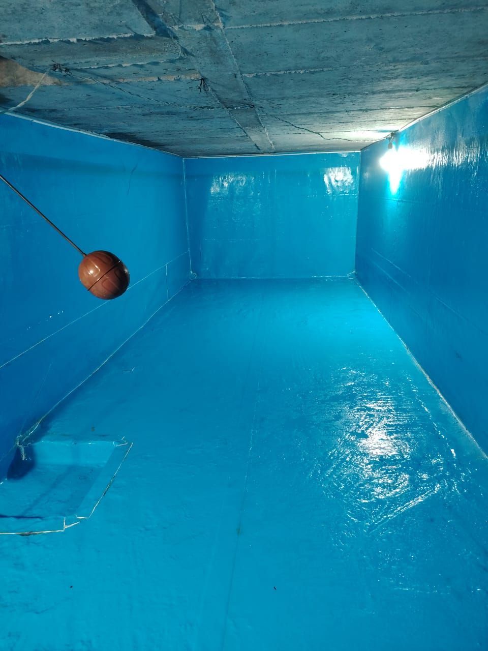 Piscina cubierta azul vacía con una pelota de baloncesto flotando cerca de la pared izquierda.
