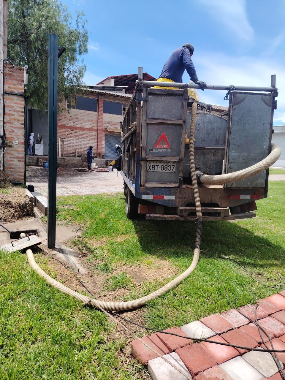 Un trabajador en un camión de servicios públicos rocía con una manguera un jardín cubierto de hierba junto a un camino de entrada de ladrillos.