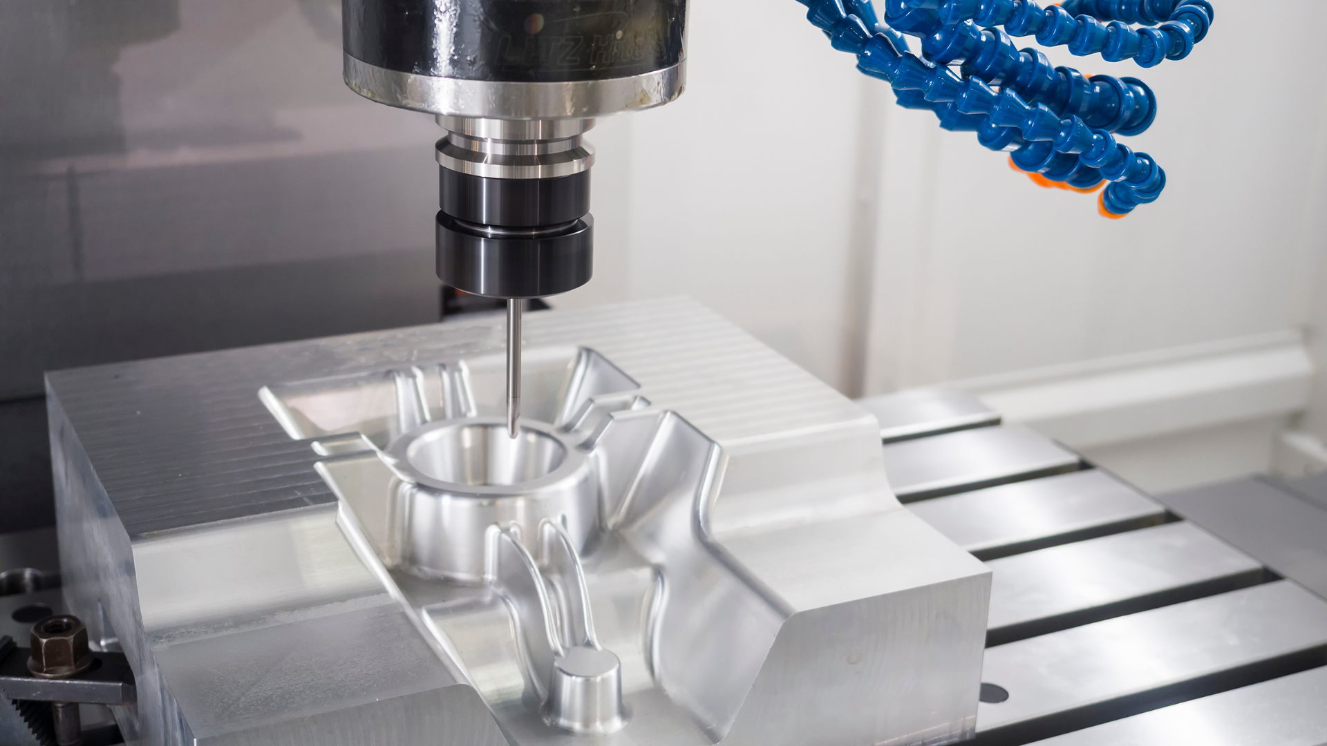 CNC milling machine cutting a metal block on a worktable with blue coolant hoses