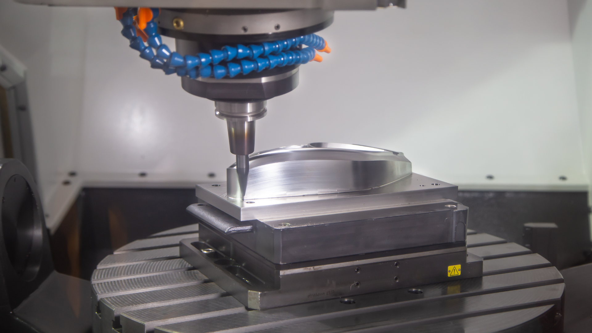 CNC milling machine cutting a metal block on a rotary table in a workshop