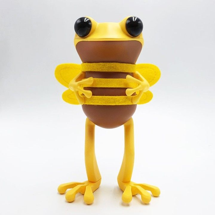 Yellow and brown frog-bee hybrid figurine with large eyes, wings, and striped torso, standing upright.