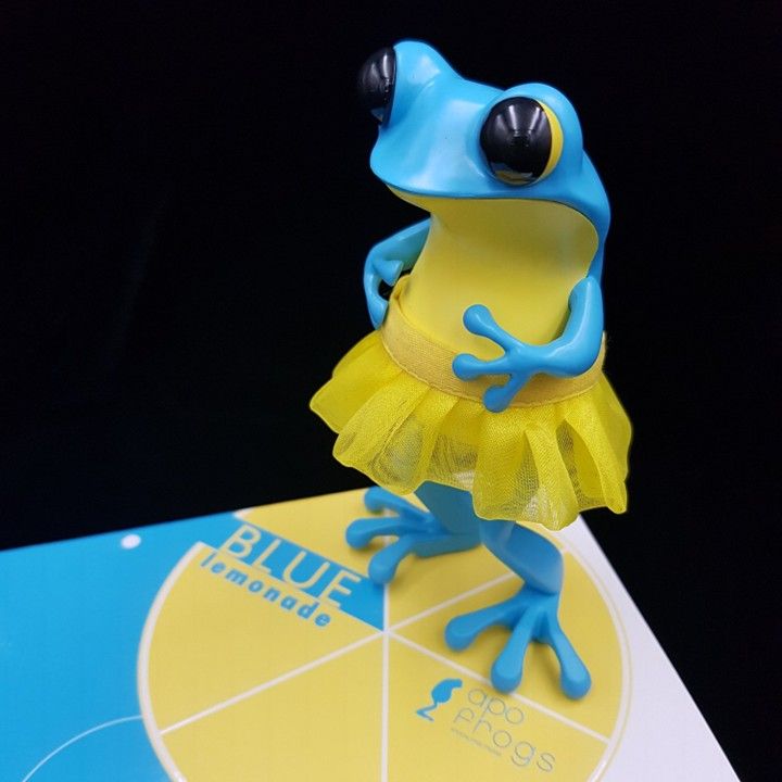 Blue frog figurine wearing a yellow tutu, perched on a 