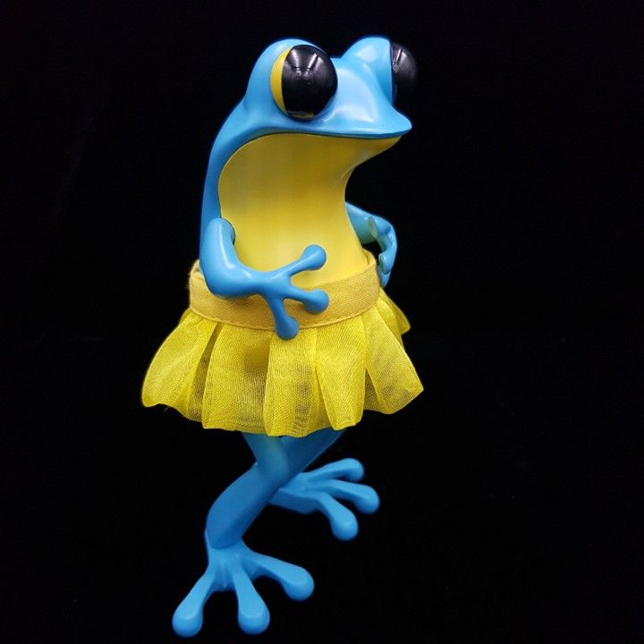 Blue frog figurine wearing a yellow tutu, perched on a 