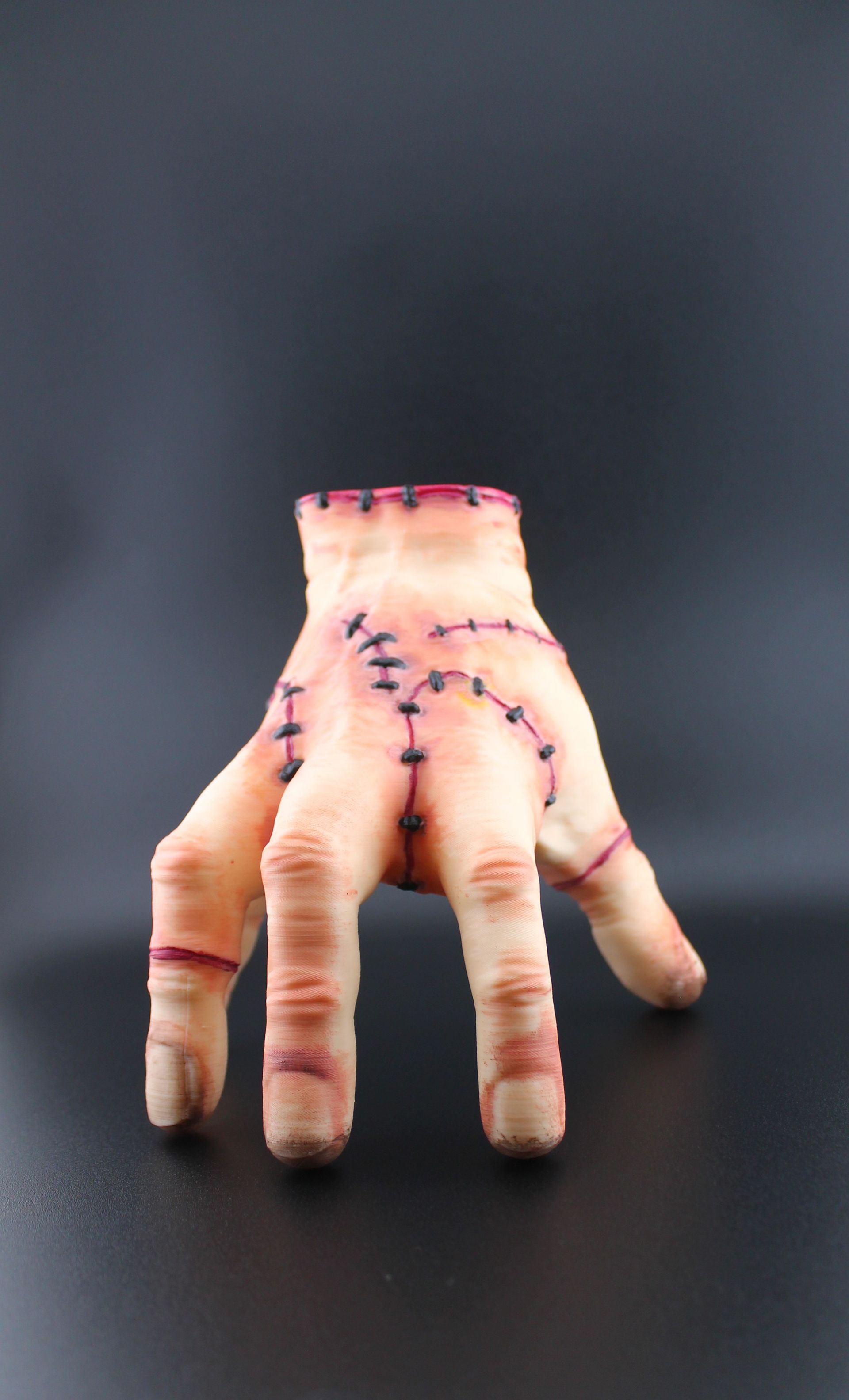 A prosthetic hand, flesh-toned with visible stitches, posed against a dark background.
