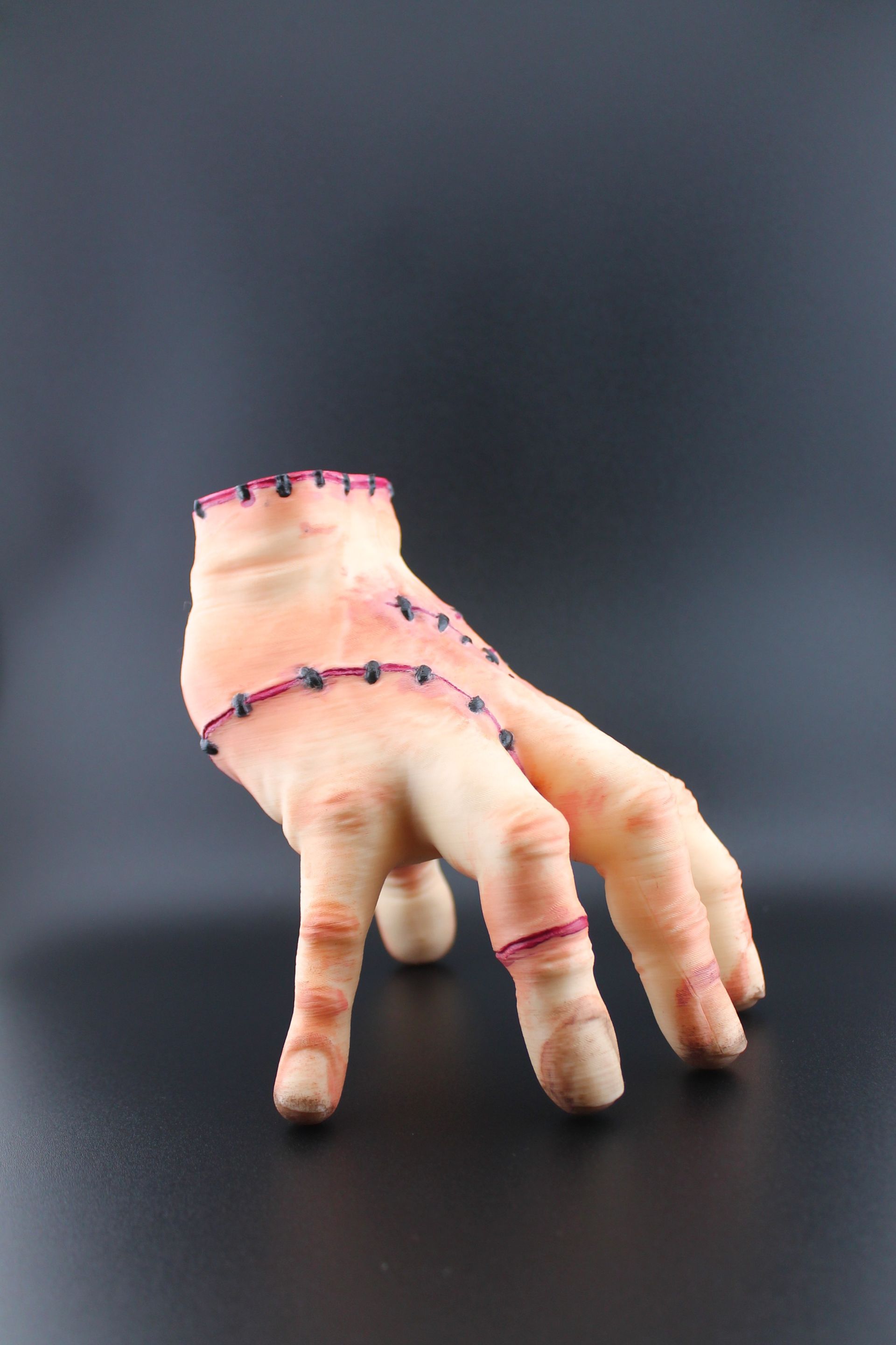 A prosthetic hand, flesh-toned with visible stitches, posed against a dark background.