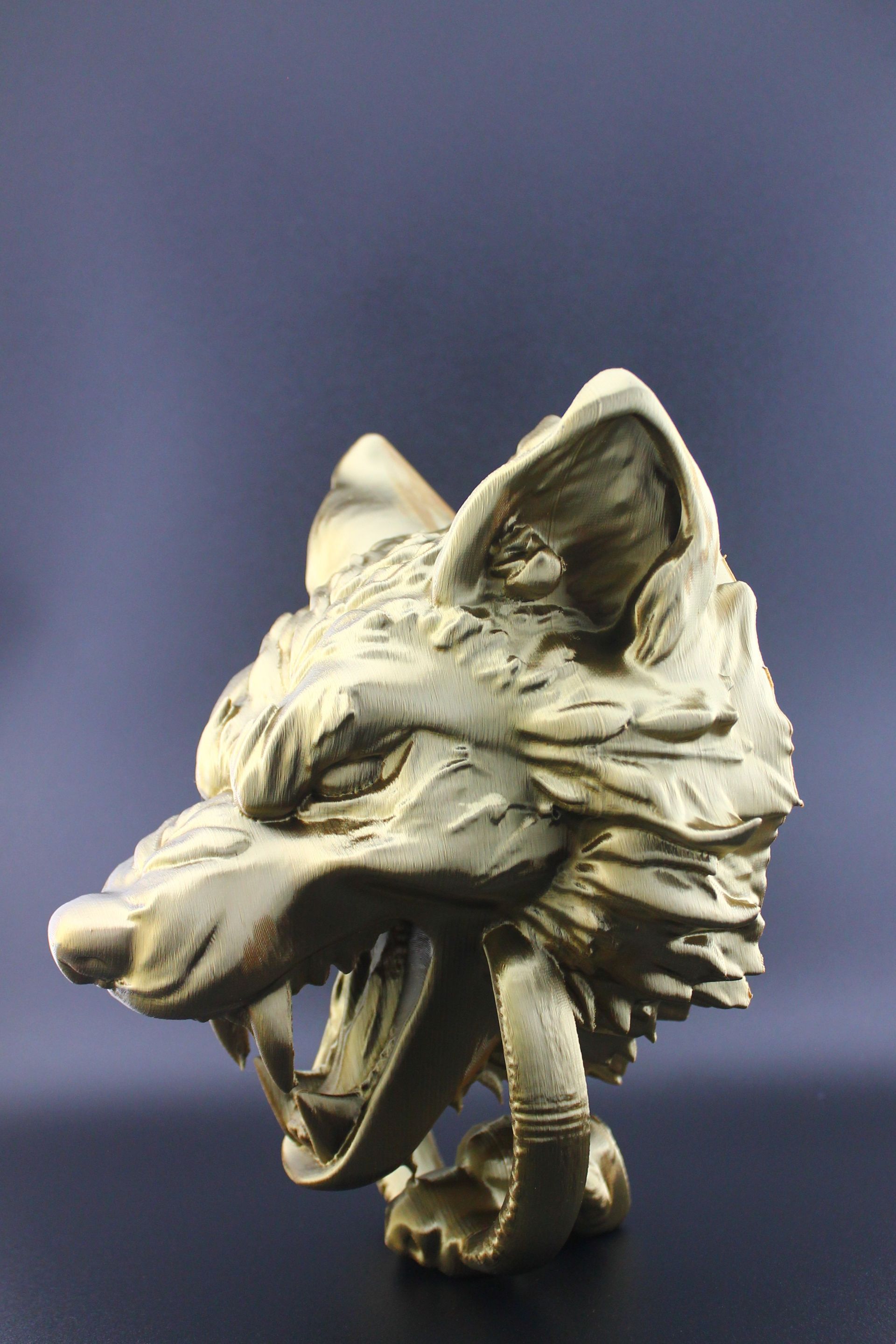 Gold-colored wolf head sculpture with snarling expression against a dark backdrop.
