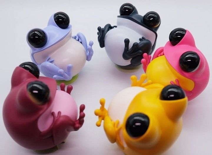 Two cartoon frog figures, one black and white, the other pink, sit on a white surface.