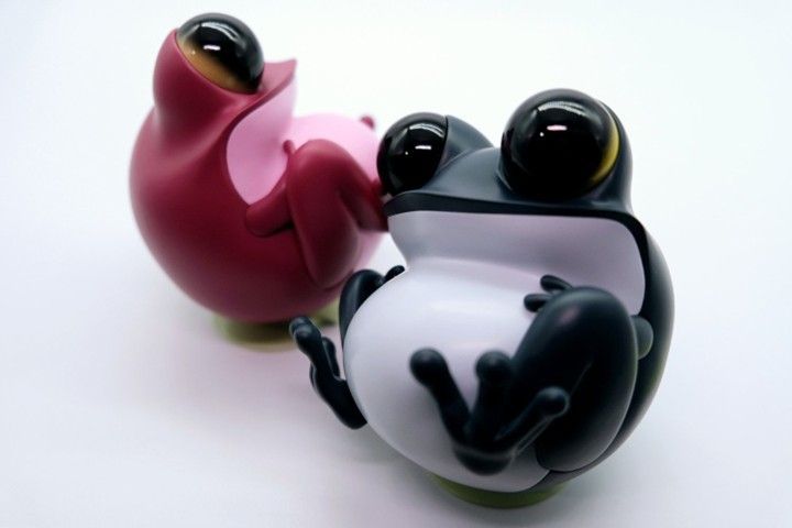 Two cartoon frog figures, one black and white, the other pink, sit on a white surface.