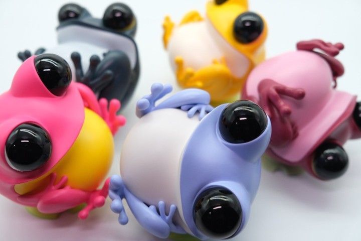 Two cartoon frog figures, one black and white, the other pink, sit on a white surface.