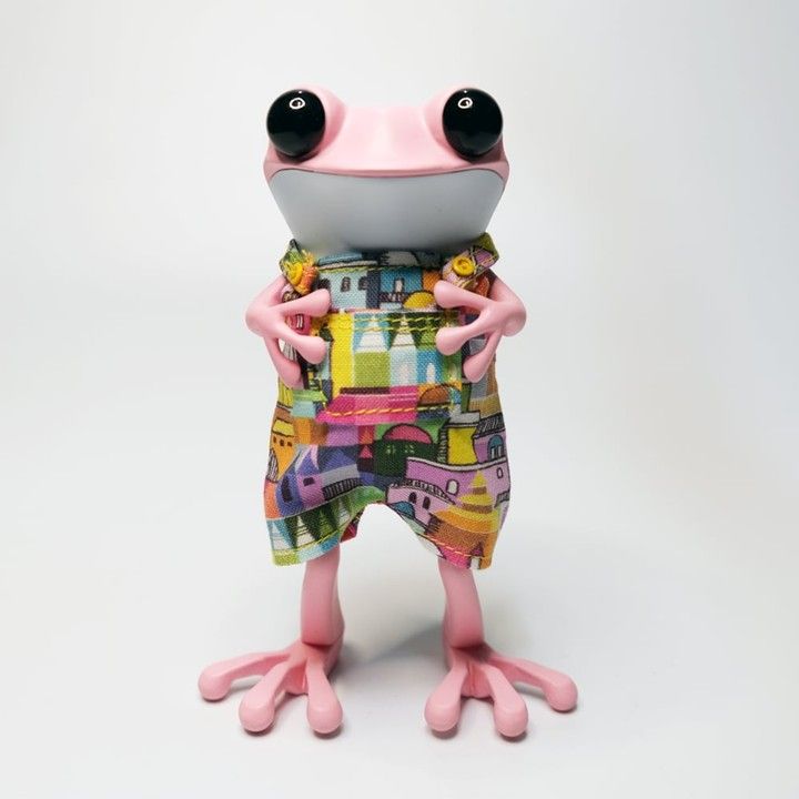 Pink frog figurine wearing colorful patterned overalls.