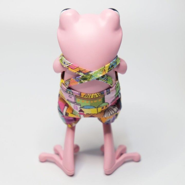 Pink frog figurine wearing colorful patterned overalls.