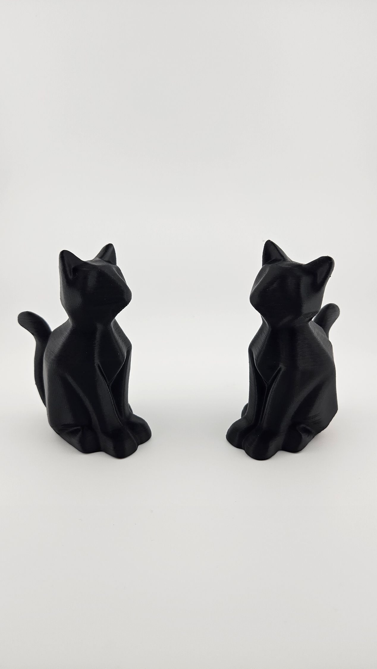 Black cat figurine, sitting upright, looking up, on a white surface.
