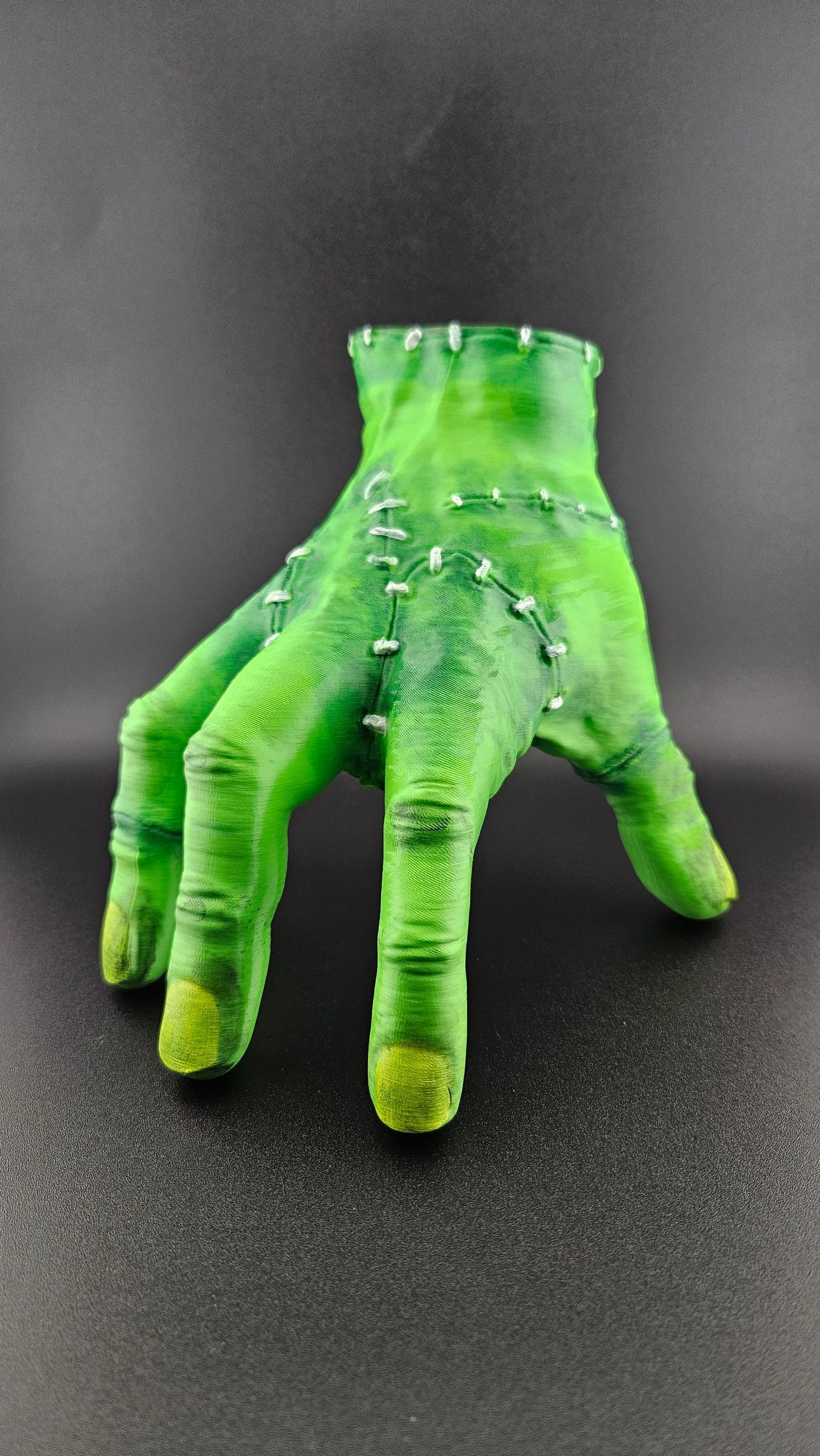 Green Frankenstein-like hand with stitches and metal studs, on a black background.