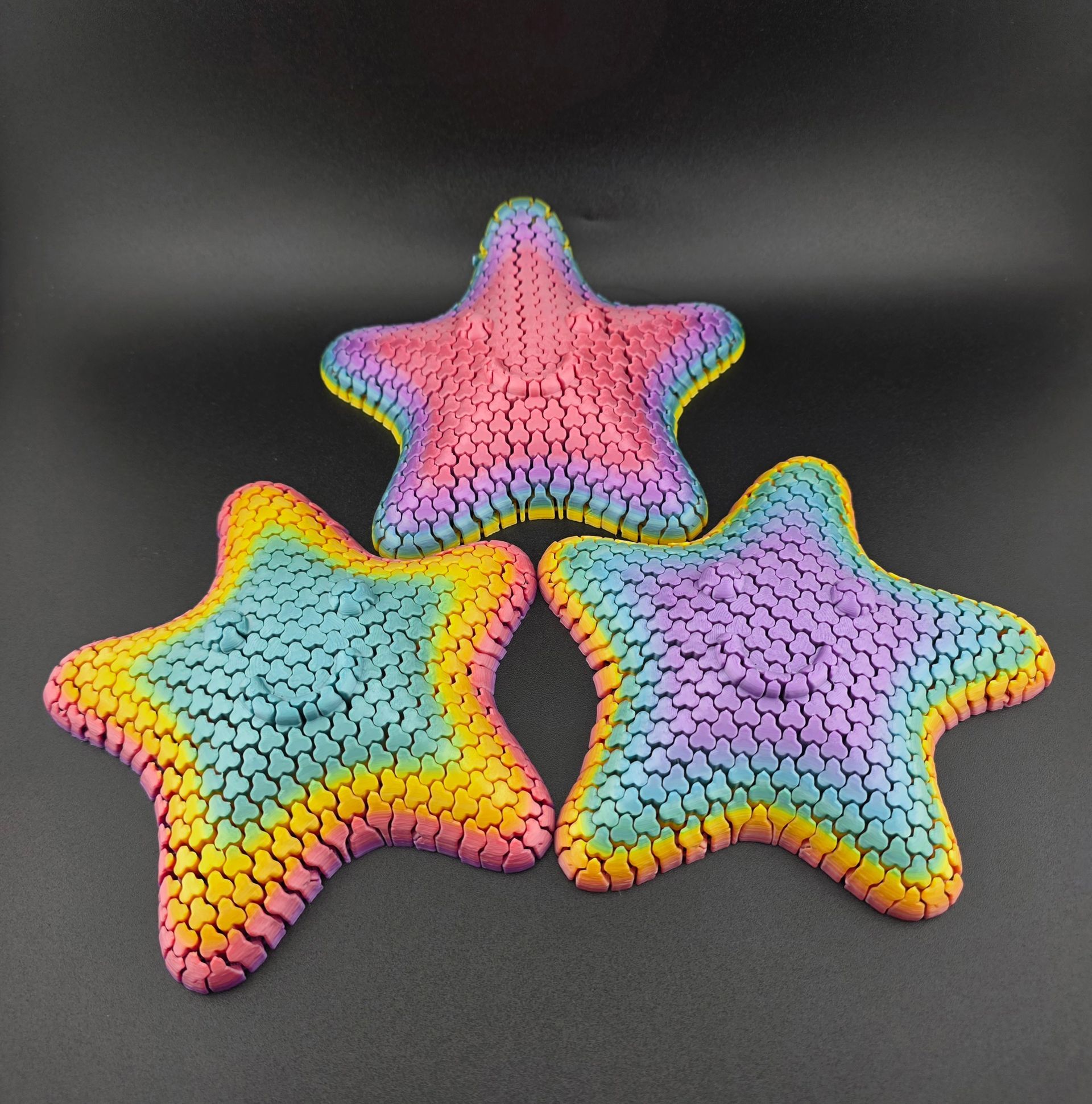 Three colorful, rainbow-hued starfish toys on a dark surface.