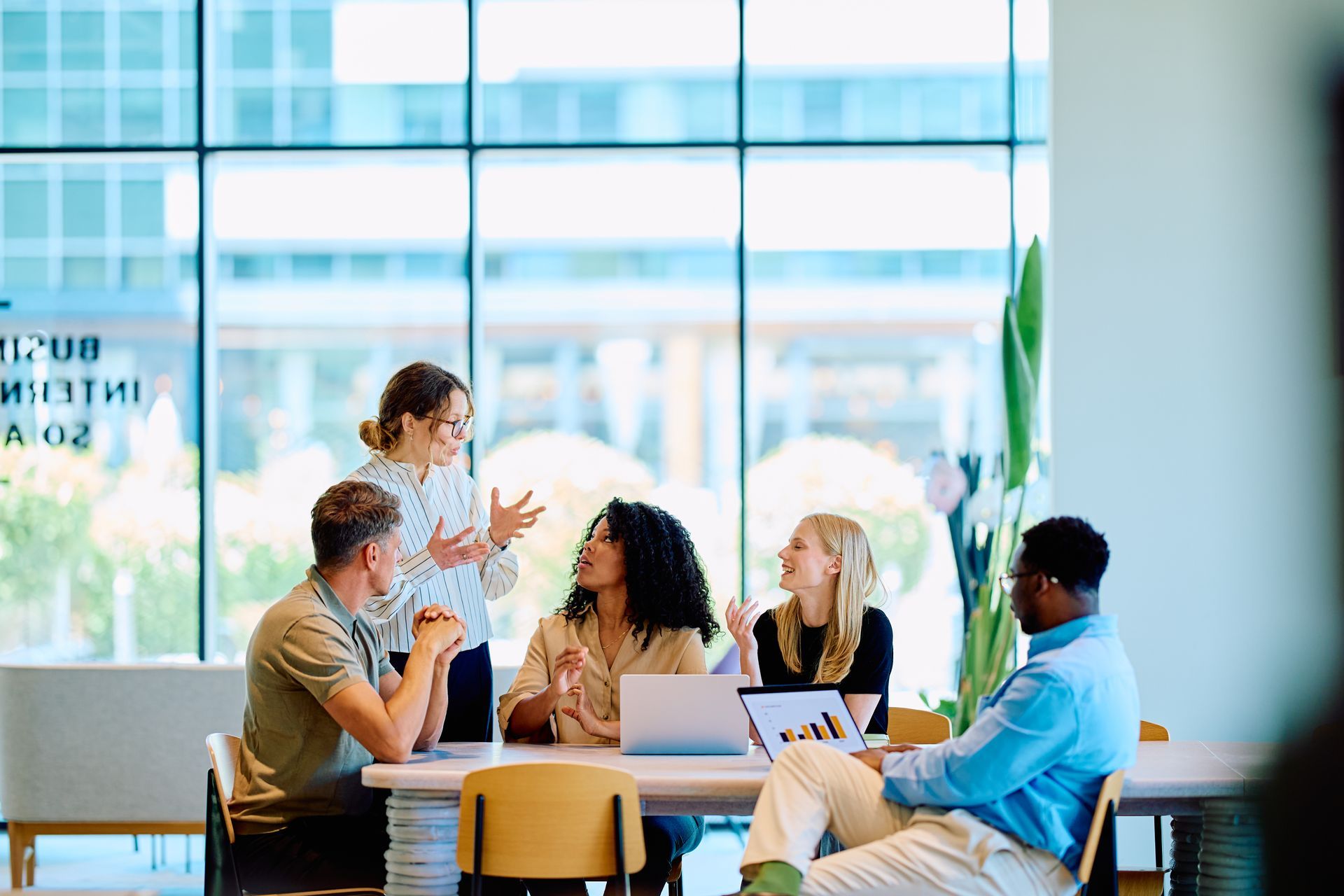 Small group meeting around a table in a bright, modern office with large windows.
