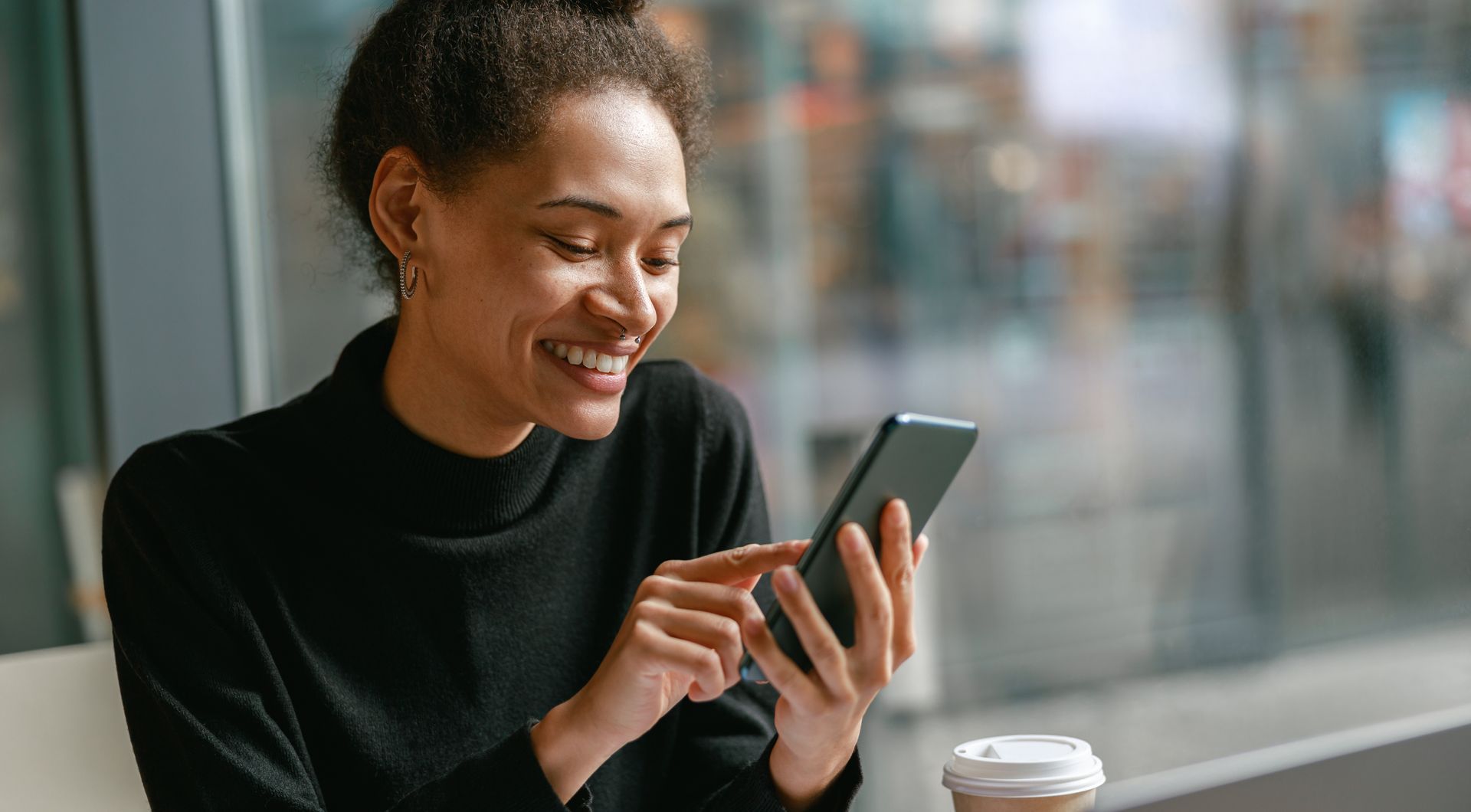 Young woman typing on phone, smiling at cafe table