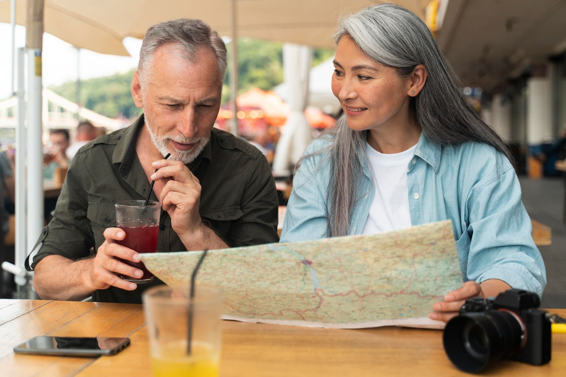 Older couple looking at phone together, laptop and documents on table.