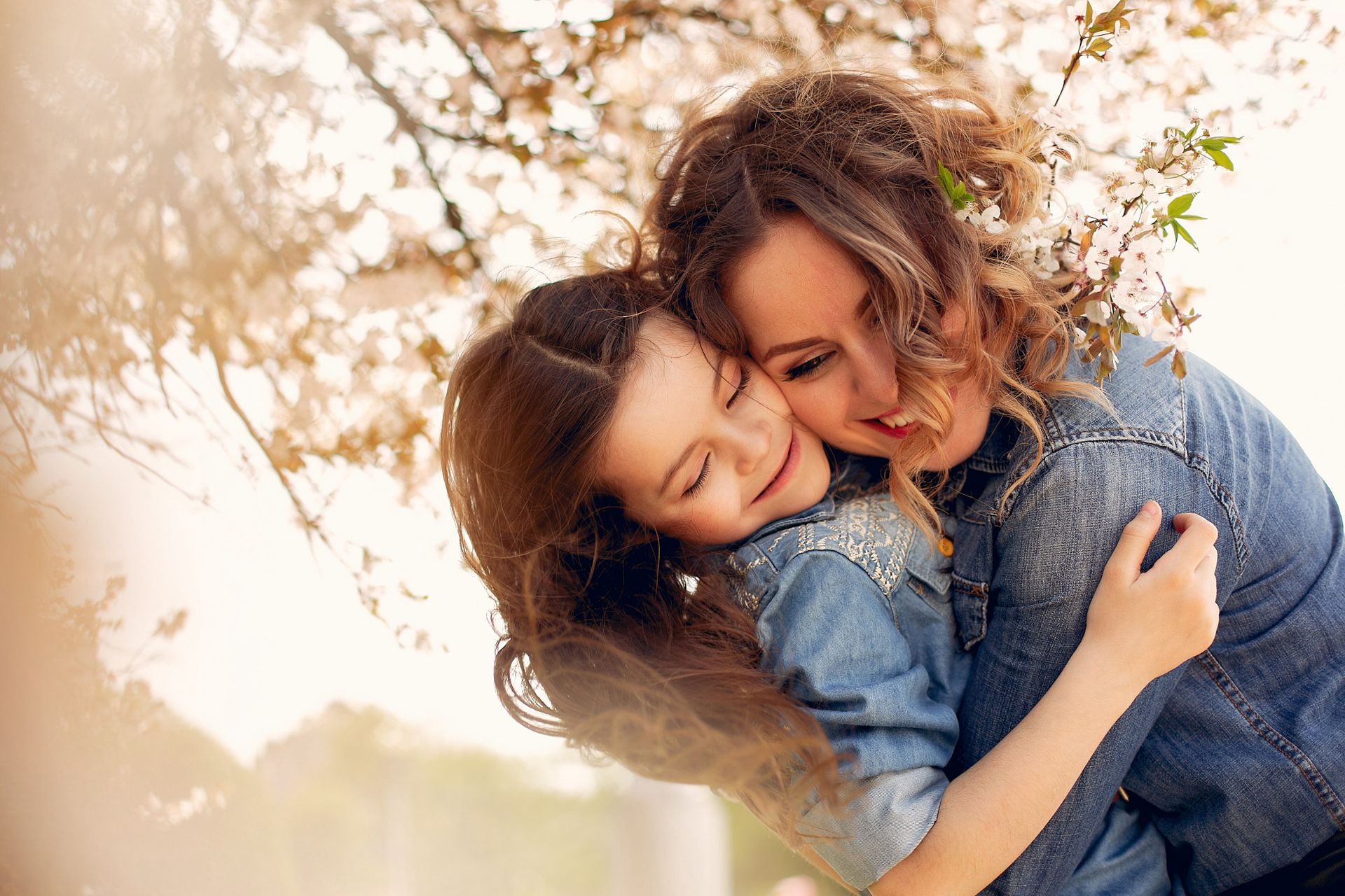Woman and child embrace under blooming tree.
