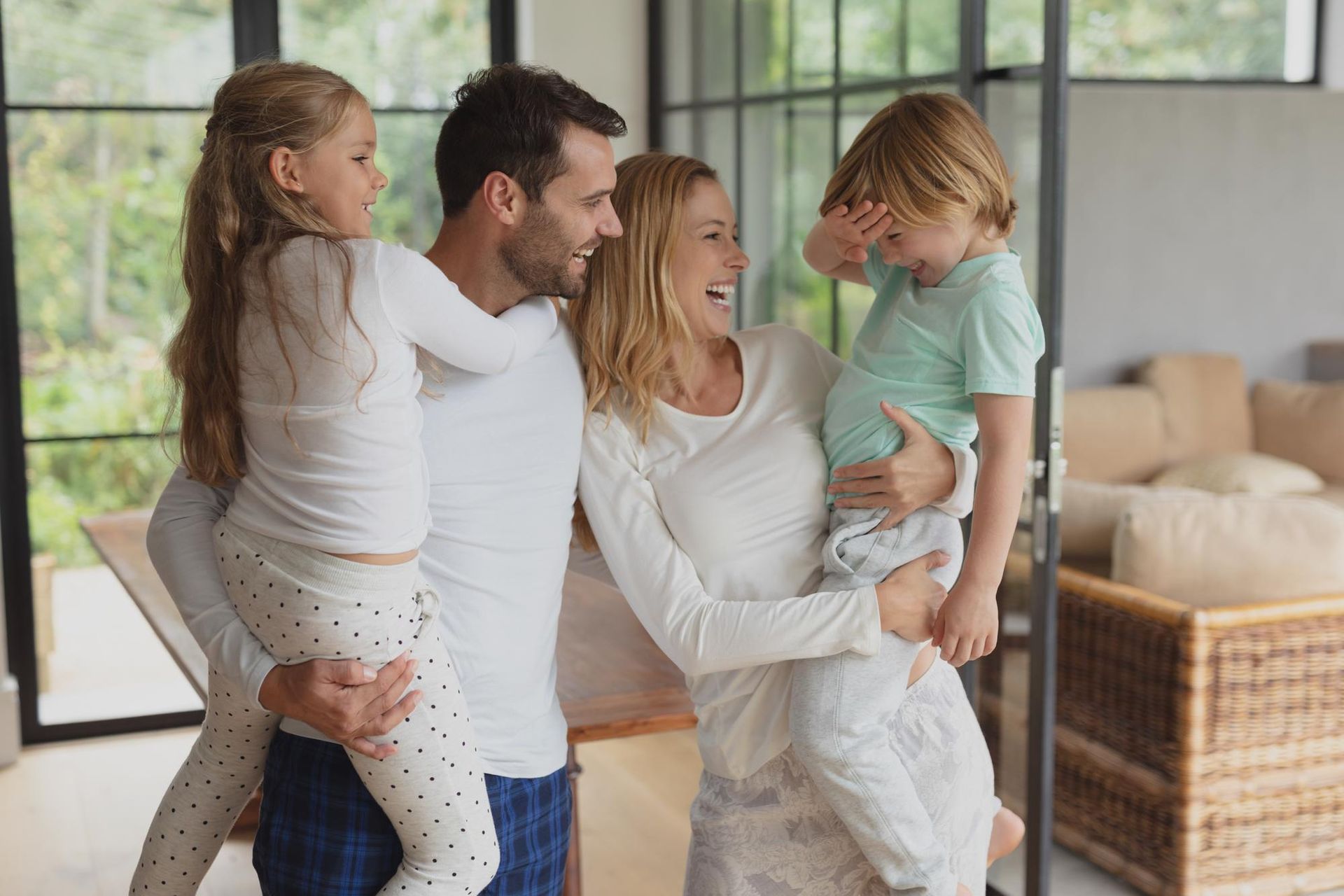 Family in a modern home, smiling and hugging. Two children are held by parents.