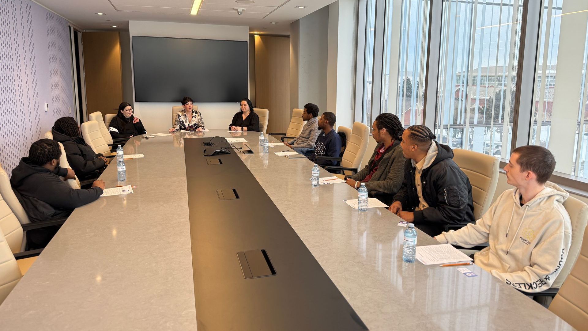 A group of people are sitting at a long table in a conference room. A group of people are sitting at a long table in a conference room.