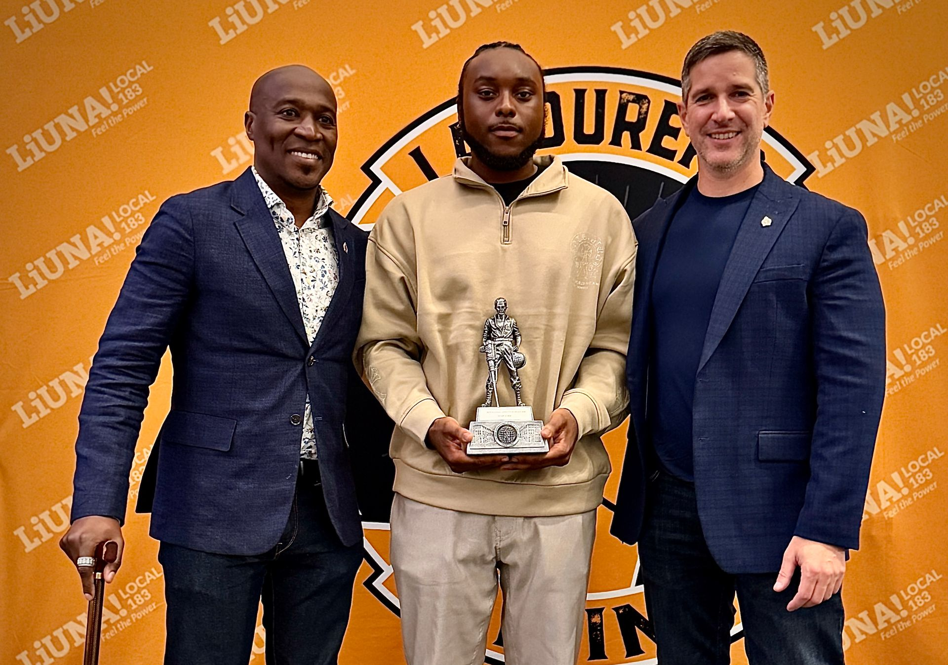 Three men pose with a trophy in front of an orange event backdrop.